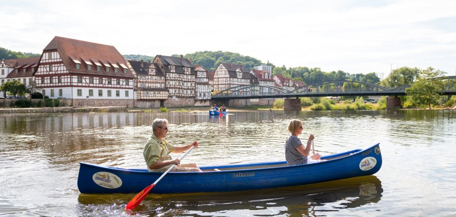Ein Kanu mit zwei Personen fahren auf der Fulda. Im Hintergrund sind Fachwerkhäuser der Stadt Rotenburg an der Fulda zu sehen.