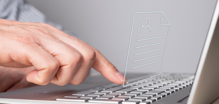 Ein silberner Laptop aus dem Seitenprofil betrachten. Eine Hand klickt mit dem Zeigefinger auf eine Taste. In der Mitte über den Laptoptasten ist ein Formular-Symbol zu sehen.
