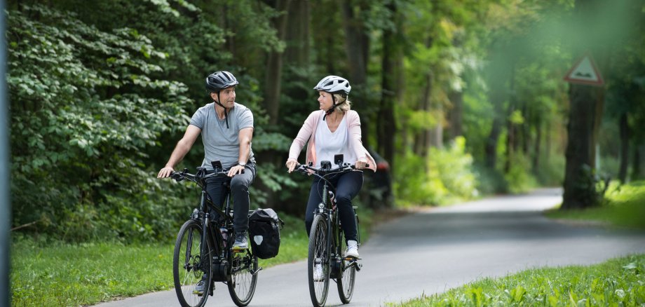 Zwei Radfahrer, ein Mann und eine Frau, fahren auf dem Fulda-Radweg R1 durch den grünen Wald.