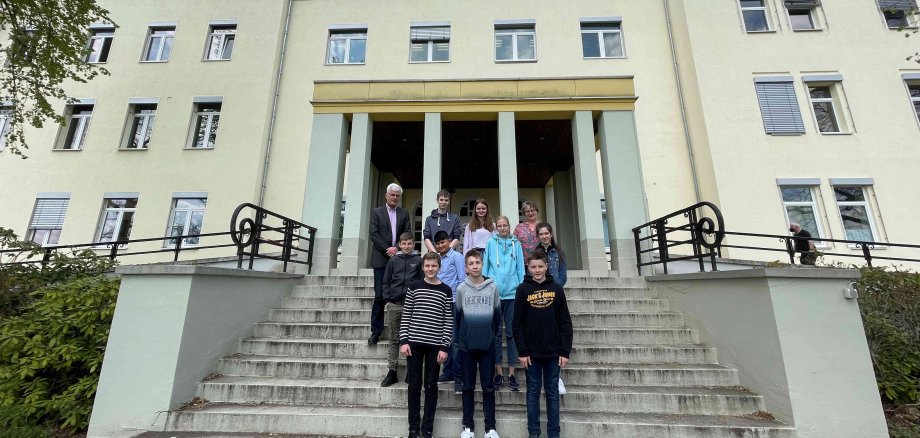 Sieben Schülerinnen und Schüler stehen mit Landrat und Ausbildungsleiterin auf der Treppe vor dem Landratsamt zum Gruppenfoto. 