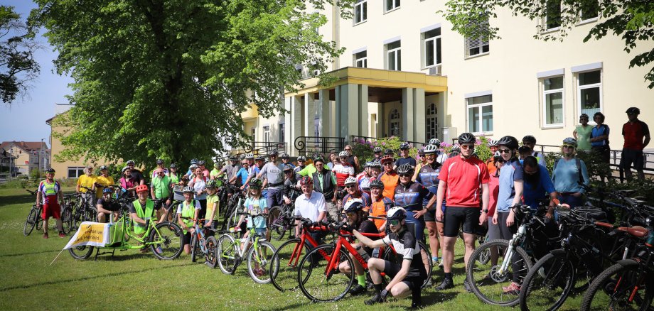 Viele Radfahrer und Radfahrerinnen stehen mit ihren Fahrrädern auf einer grünen Wiese vor dem Landratsamt.