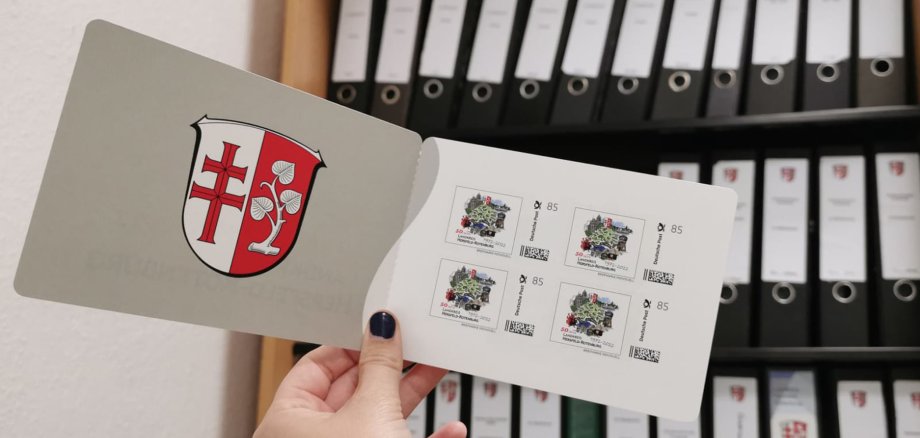 Ein Heft mit den Jubiläumsbriefmarken des Landkreises vor einem Schrank mit vielen Ordnern. Auf den Briefmarken zum 50-jährigen Jubiläum ist eine Grafik des Landkreises abgebildet.