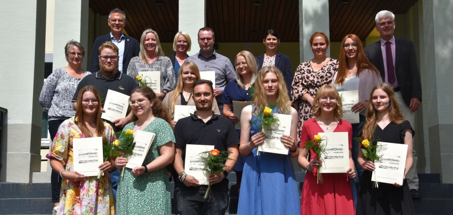 Die ausgelernten Azubis und die Absolventen von Studium und Fortbildung stehen gemeinsam mit der Kreisspitze und Personalvertretungen sowie Ausbildung- und Personalleitung auf der Treppe vor dem Landratsamt. Sie haben ihre Urkunden und Blumen in der Hand. 