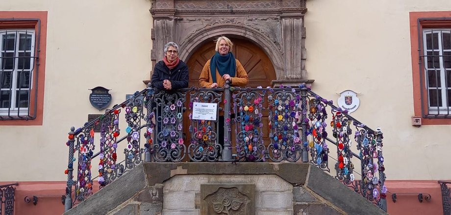 Zwei Frauen stehen auf den Treppen des Rotenburger Rathauses. Das Geländer ist mit vielen bunten, gehäkelten Blumen verziert.