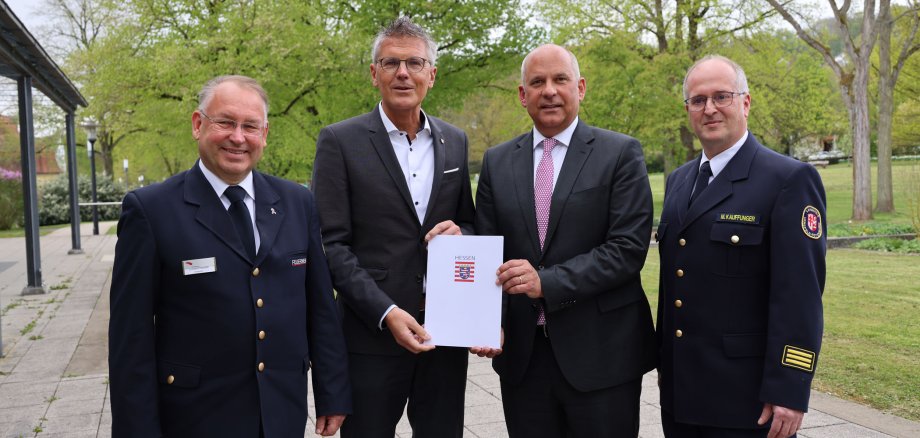 Vier Männer stehen im Kurpark in Bad Hersfeld. Die beiden Männer in der Mitte halten gemeinsam eine Mappe mit dem Logo des Landes Hessen.