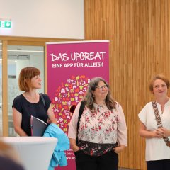 Drei Frauen stehen im Kreistagssitzungssaal im Landratsamt. Im Hintergrund steht ein Roll-Up der App Integreat.