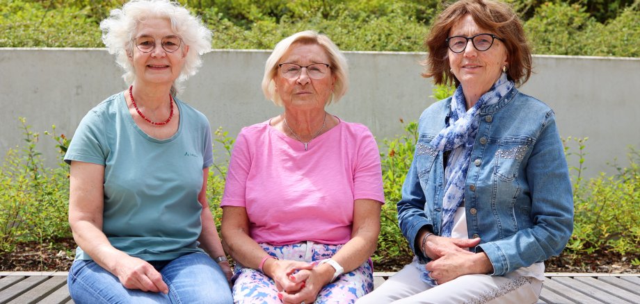 Drei Ehrenamtliche Frauen des Projekts „Hand in Hand“ – Birgit Hillert, Renate Lissek und Helga Hildebrand – sitzen nebeneinander auf einer Bank im Freien. Sie lächeln in die Kamera.