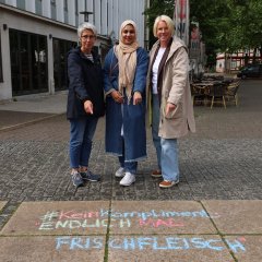 Die beiden Frauen- und Gleichstellungsbeauftragten und ihre Praktikantin stehen am Linggplatz in Bad Hersfeld und zeigen auf einen Spruch, der mit Kreise auf den Boden gezeichnet wurd. Dort steht: "#KeinKompliment: Endlich mal Frischfleisch".