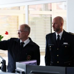 Kreisbrandinspektor Marco Kauffunger (links) zeigt mit ausgestrecktem Arm auf einen Punkt, während er mit Marco Schweitzer, Leiter der Polizeidirektion Hersfeld-Rotenburg (rechts), und zwei weiteren Personen spricht. Die Szene spielt in einem Büro mit grünen Pflanzen und Fenstern, durch die Tageslicht einfällt.