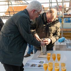 Landrat Torsten Warnecke verschließen eine glänzende Metall-Zeitkapsel. Vor ihnen auf dem Tisch stehen mehrere Gläser mit Orangensaft.