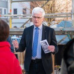 Landrat Torsten Warnecke hält ein Blatt Papier in der Hand und spricht vor einer Baustelle. Anke Hofmann steht mit dem Rücken zur Kamera.