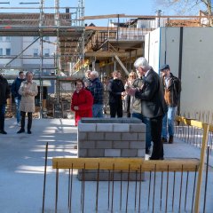 Eine Gruppe von Menschen klatscht, während die Zeitkapsel in der Betonkonstruktion versenkt wird.