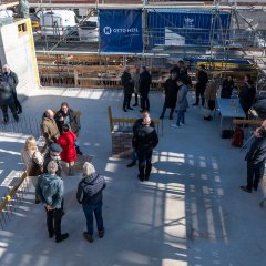 Die Baustelle von oben aufgenommen, mehrere Gruppen von Menschen stehen verteilt um die Zeitkapsel herum.